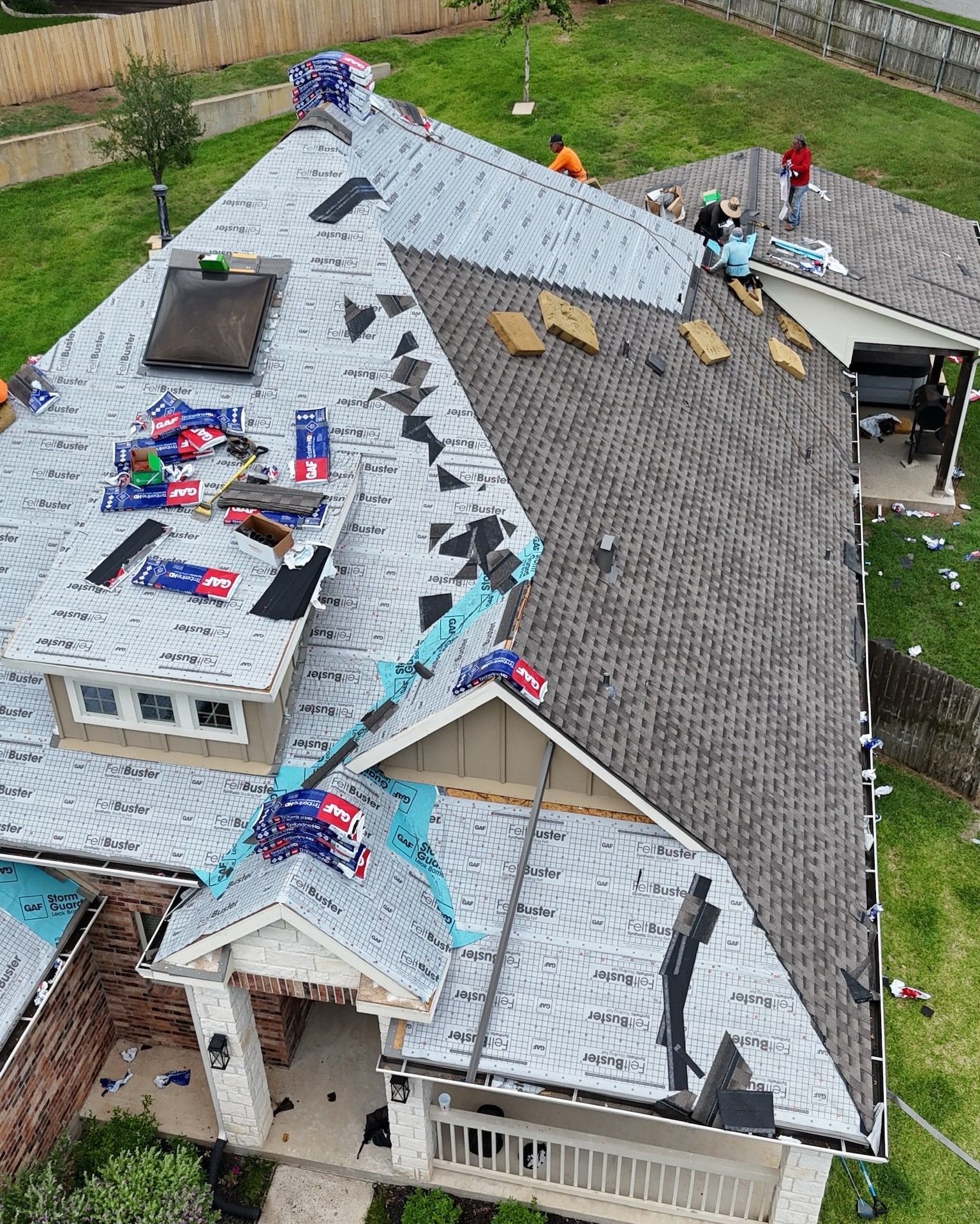 Roof being replaced on a house; workers on roof with shingles and debris.