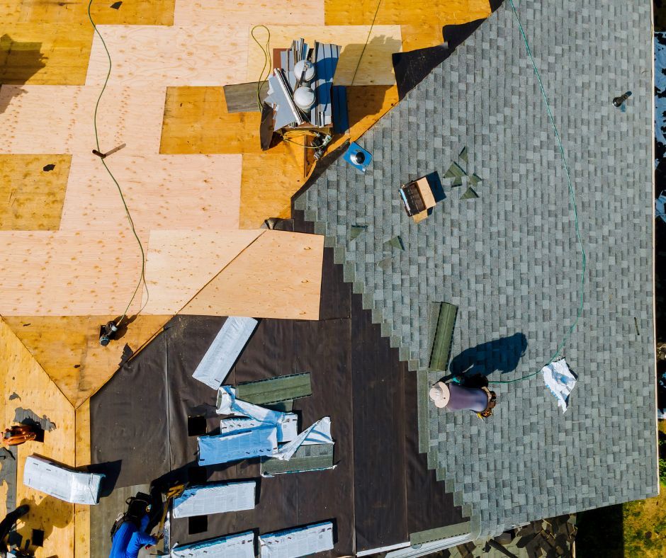 Roof being repaired; workers installing shingles on a house roof.