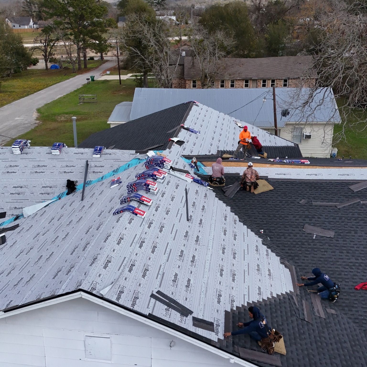Roofers installing shingles on a multi-section roof with various stages of completion.
