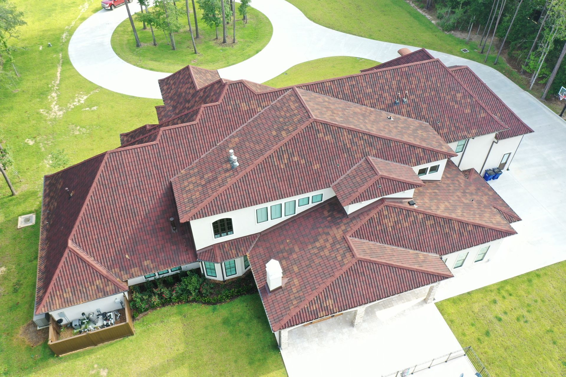 Aerial view of a large brown-roofed house with a circular driveway and surrounding green grass.