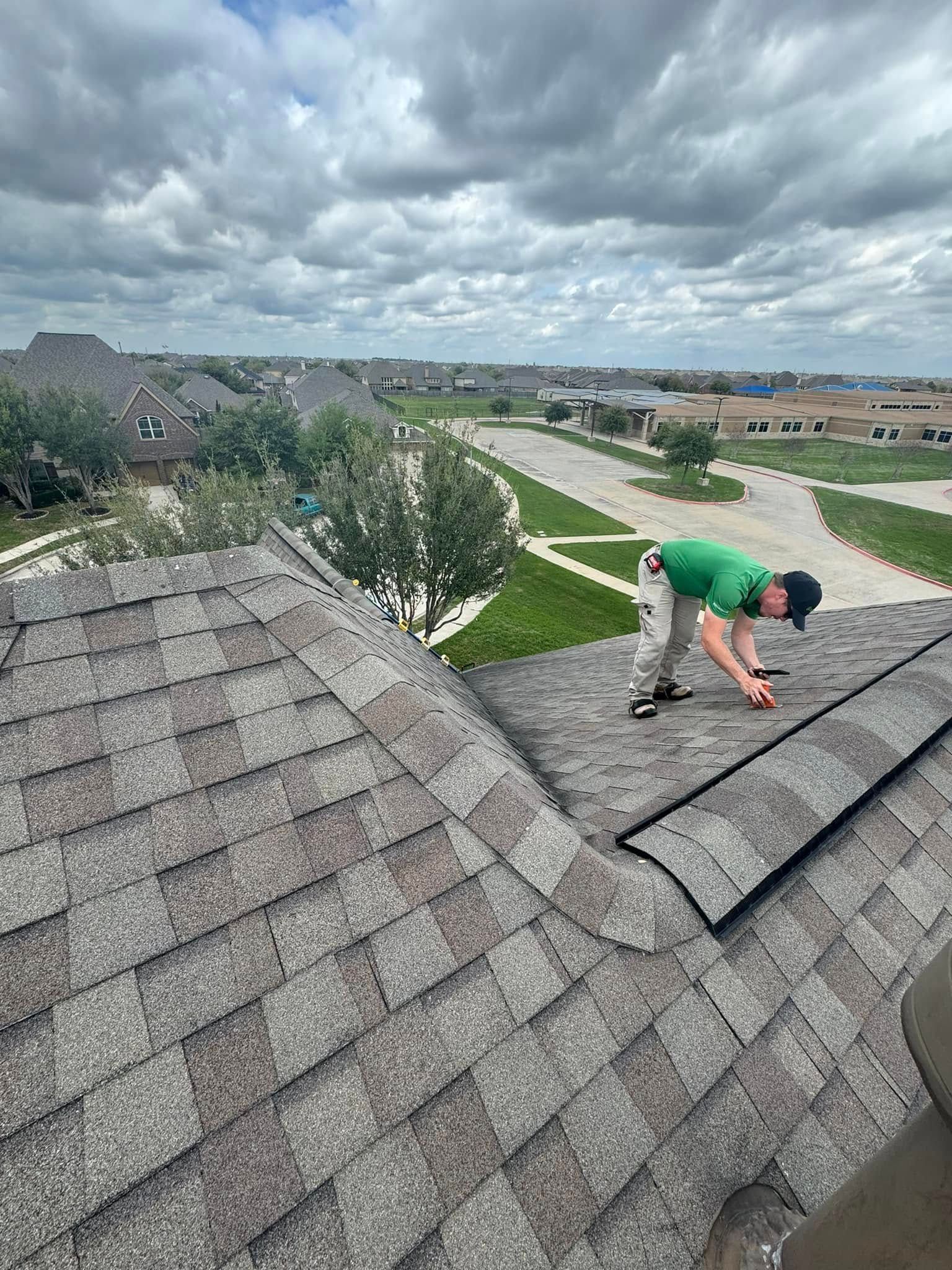 Person on a roof inspecting shingles on a cloudy day in a suburban neighborhood.