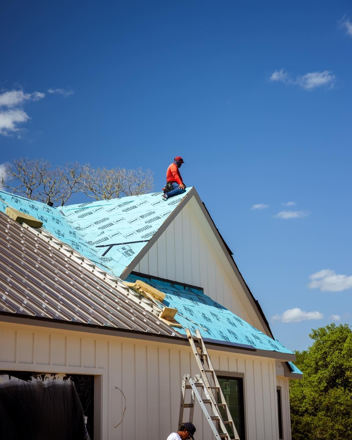 Roofer on a house roof under construction, installing blue underlayment on a sunny day.