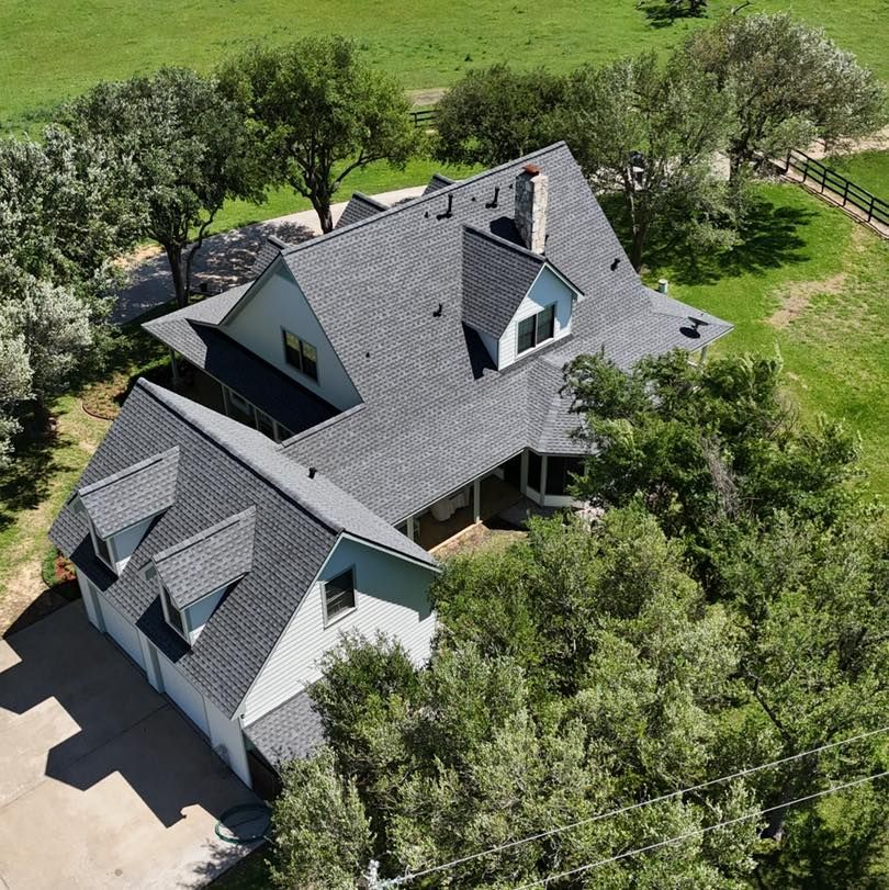 Overhead view of a house with a gray roof, surrounded by trees and green grass.
