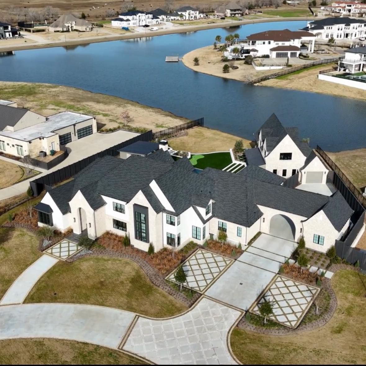 Aerial view of a large house with a long driveway next to a lake.