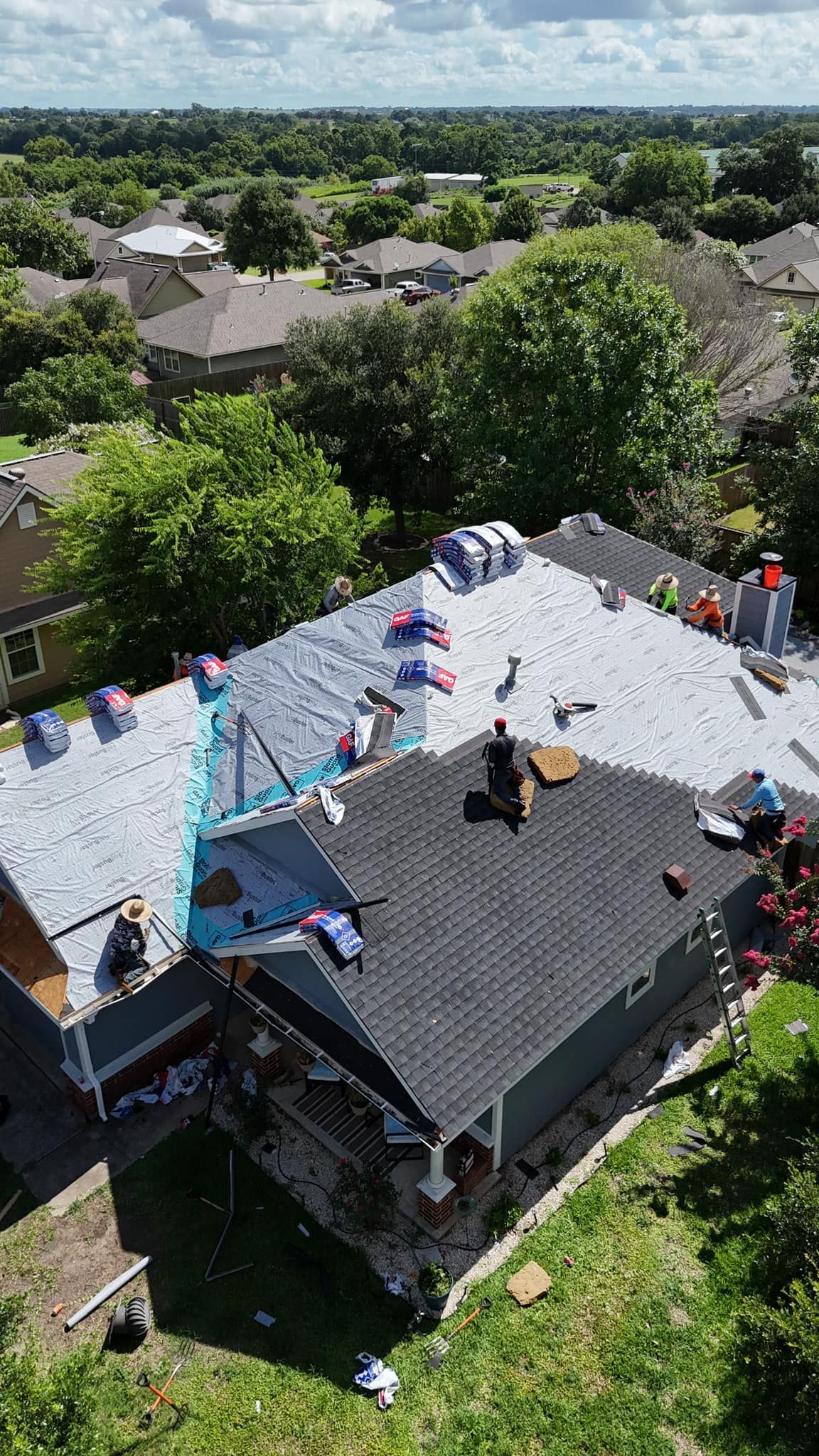 Roofing crew working on a house roof replacement; surrounded by trees.