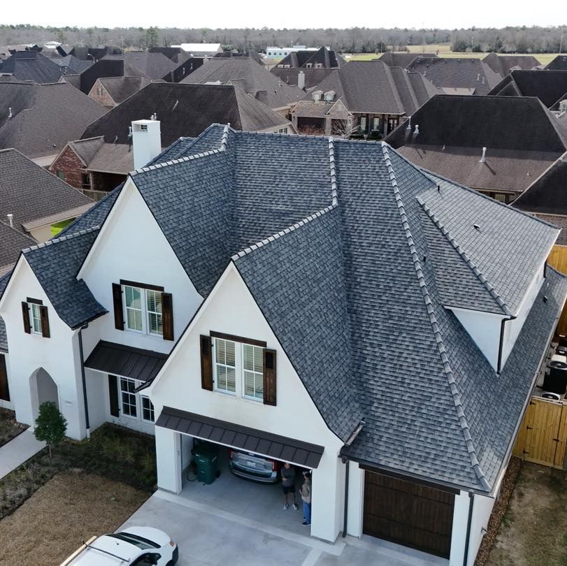 White house with a dark gray roof in a neighborhood. Garage door open; a car is visible.