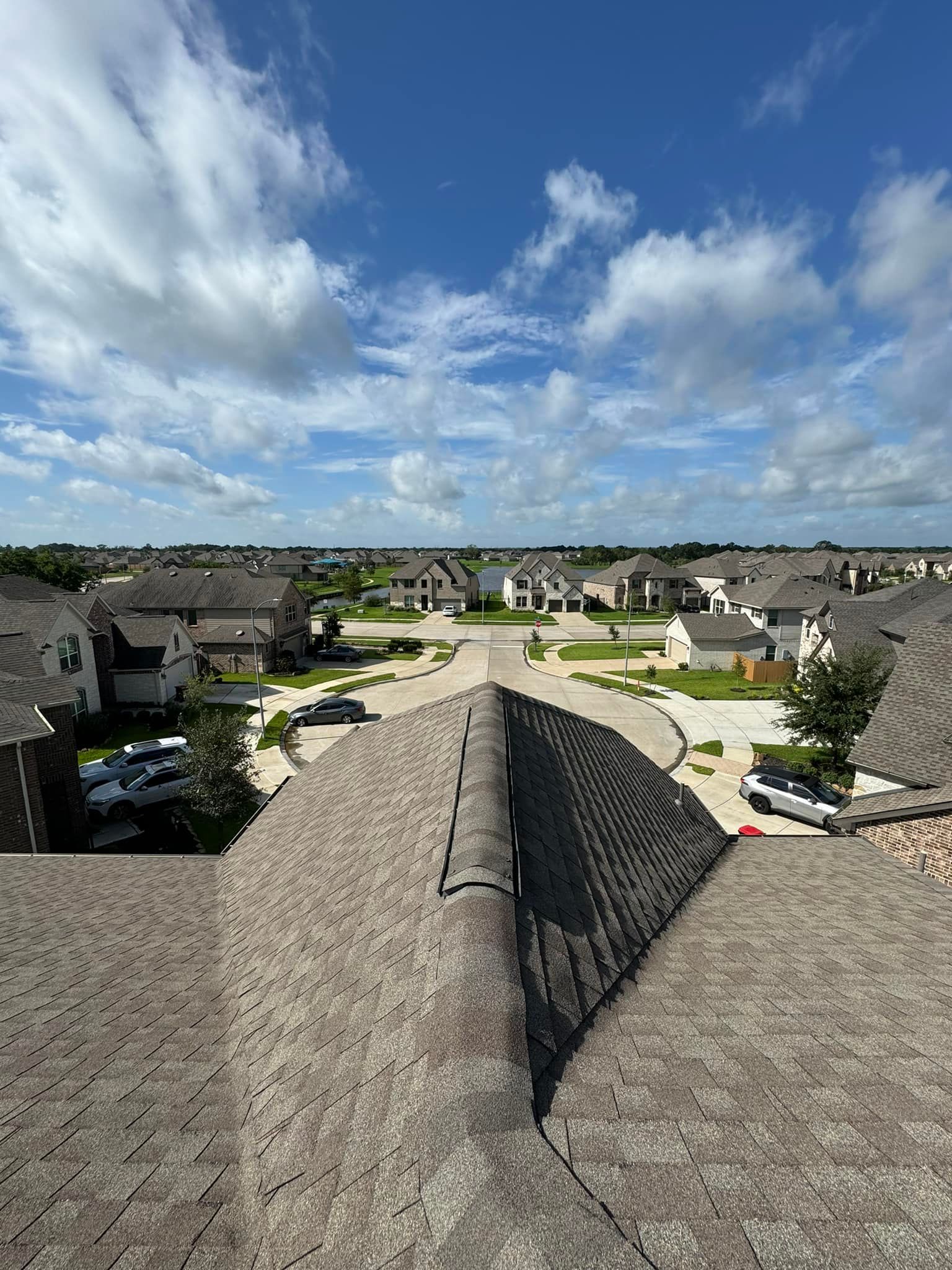 Overhead view of rooftops in a residential area under a blue sky with fluffy clouds.