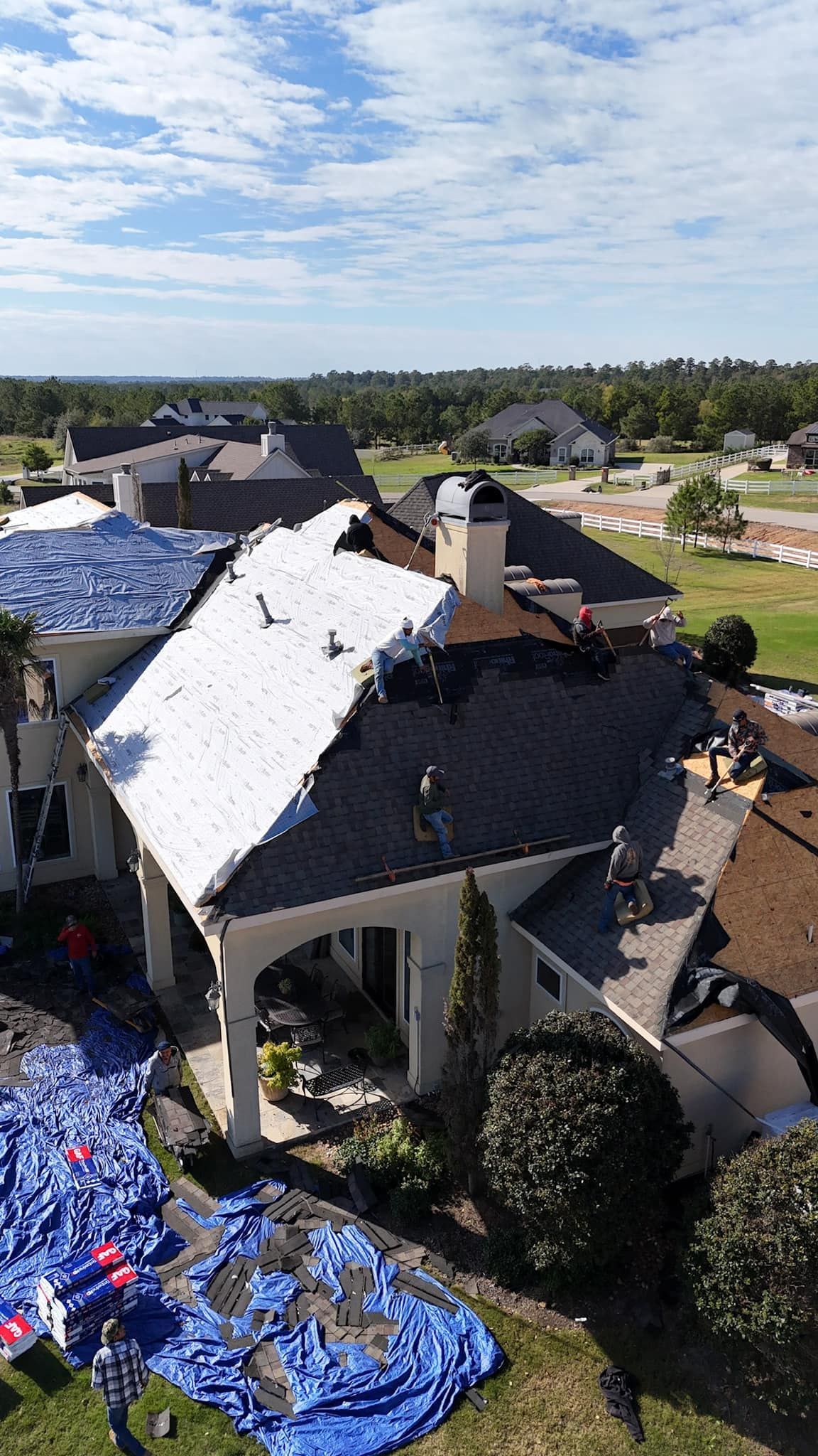 Roof partially covered with tarp; workers on roof; debris on ground.