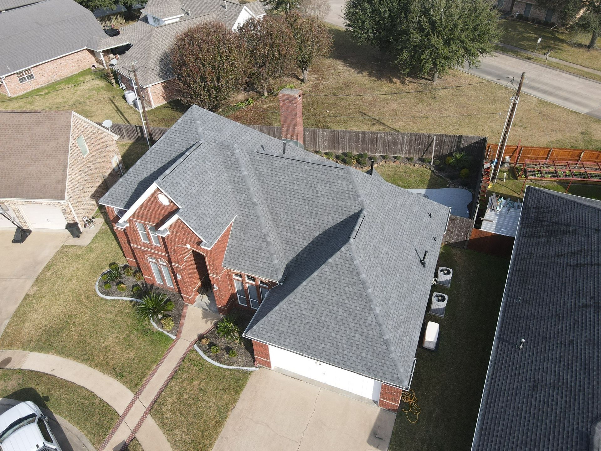 Overhead view of a red brick house with gray roof, surrounded by lawn and driveway.