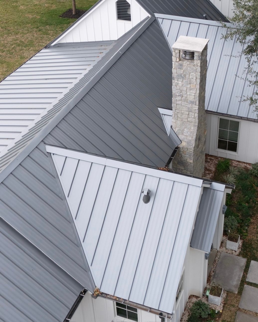 Gray metal roof of a house with a stone chimney and white trim.