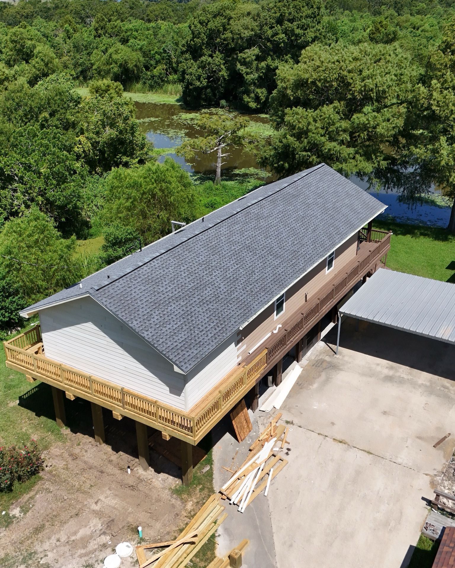 A two-story house with a wooden deck. The house is surrounded by trees and a pond.