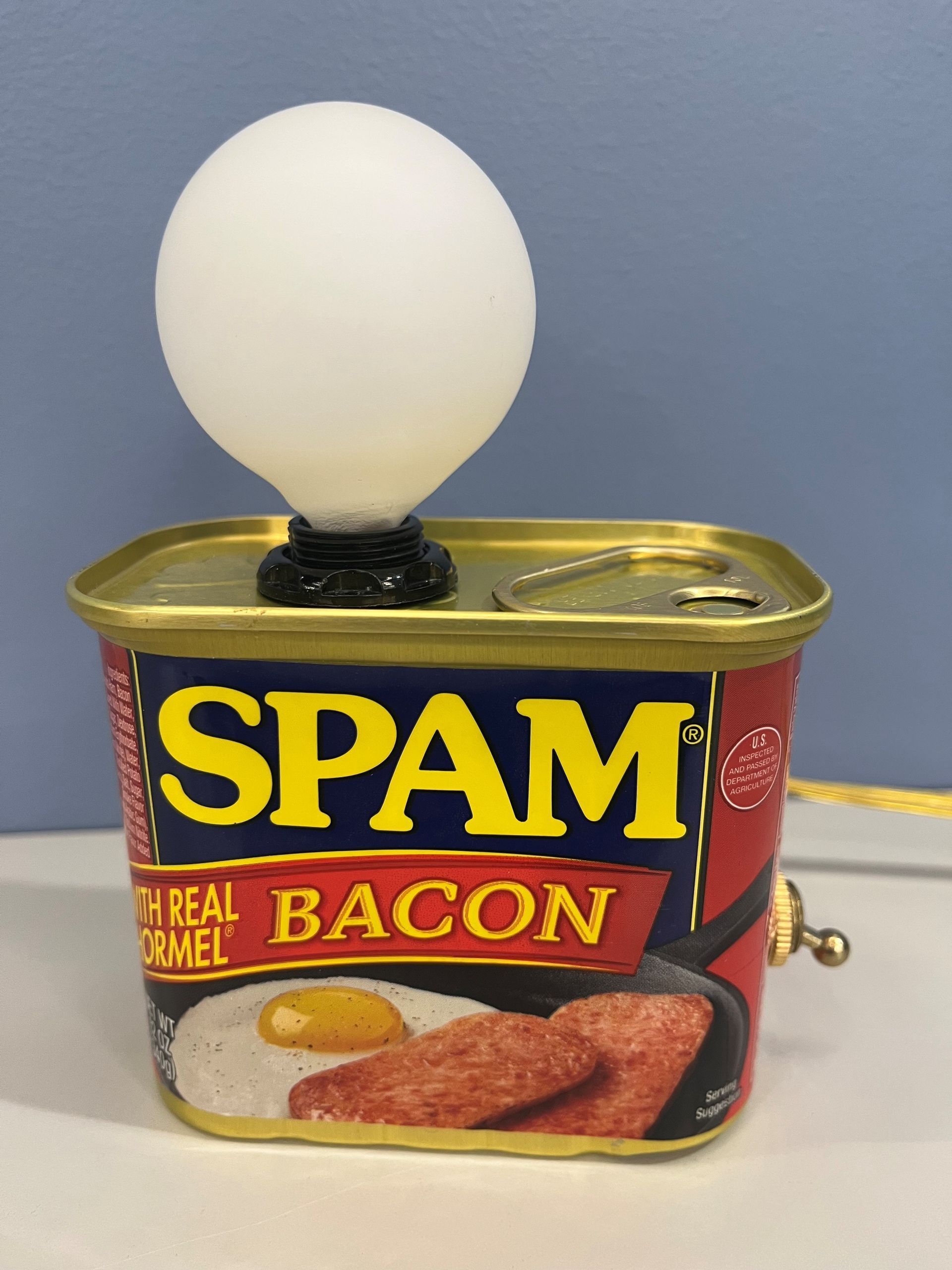 Spam can repurposed as a lamp, with a lightbulb on top and a switch on the side.