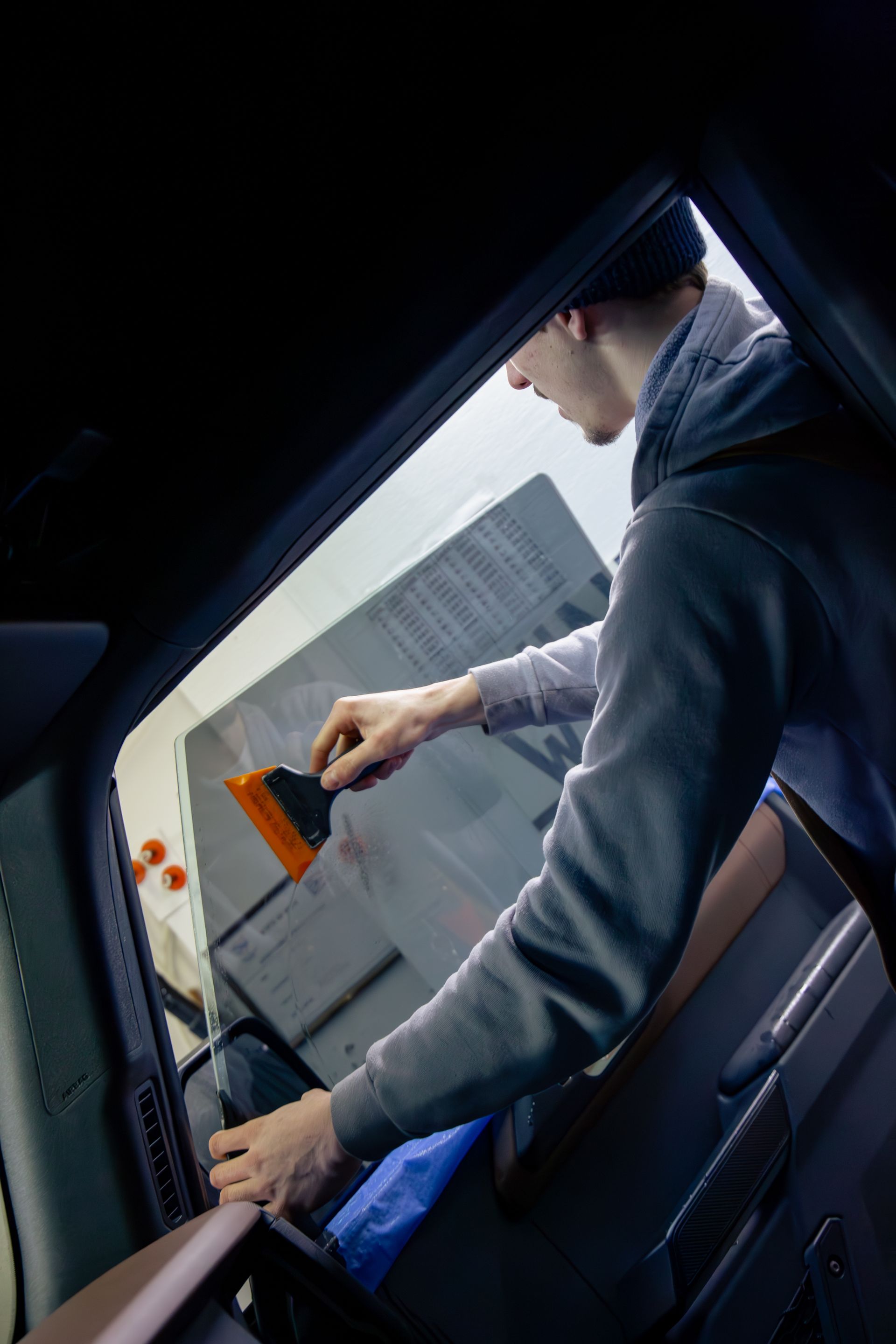 Person applying tint to a car window with a squeegee inside a car.