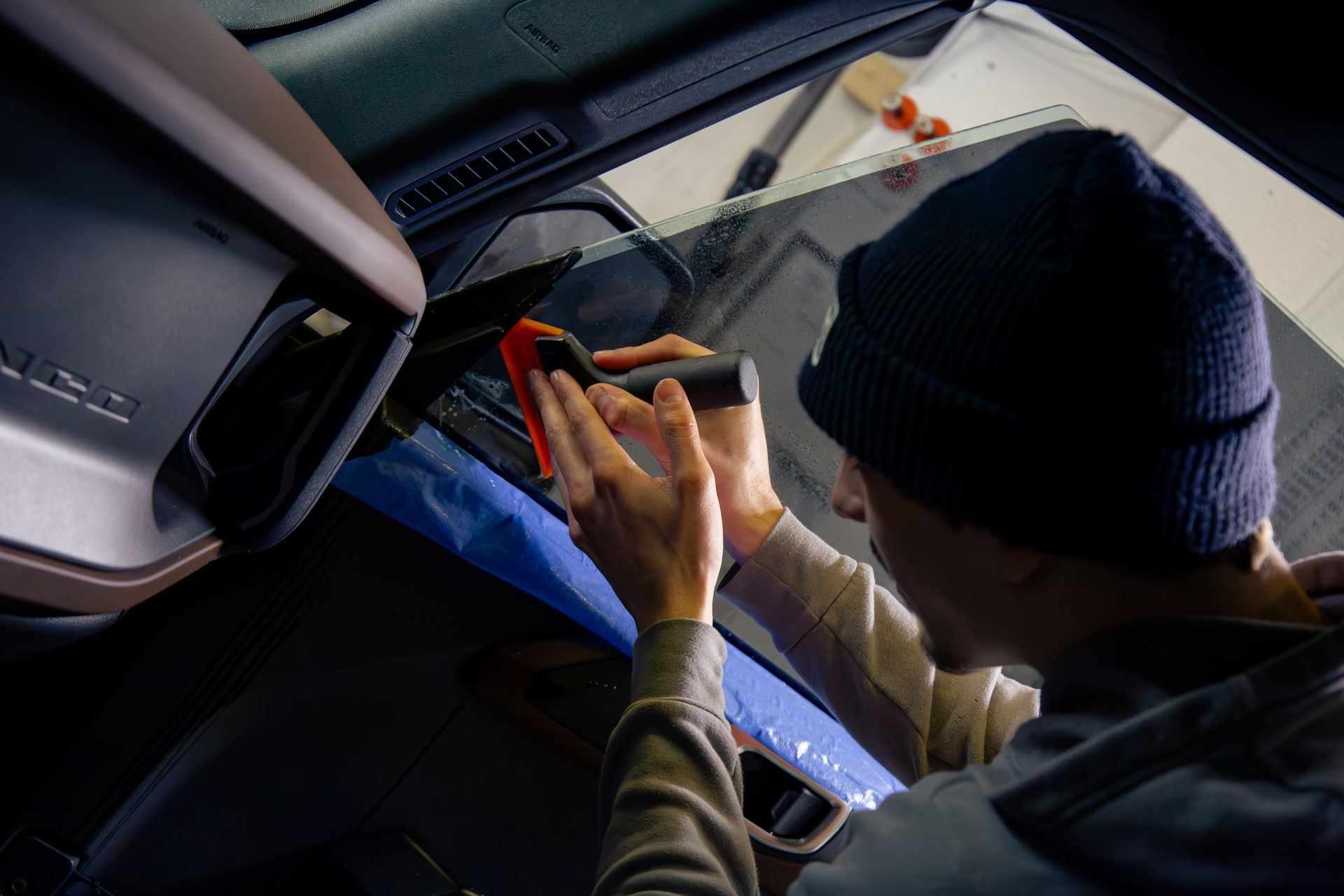 Person applying tint to a car window with a tool, inside a vehicle.