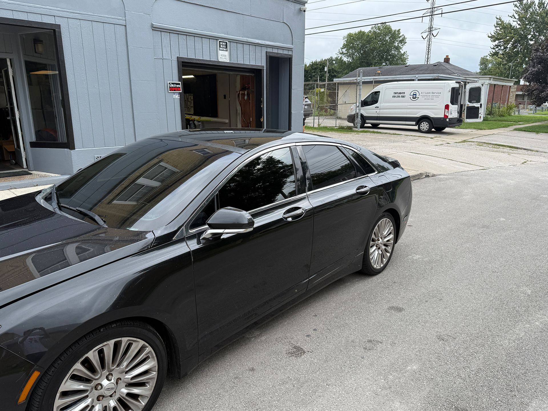 Black sedan parked outside a building with tinted windows. A service van is in the background.