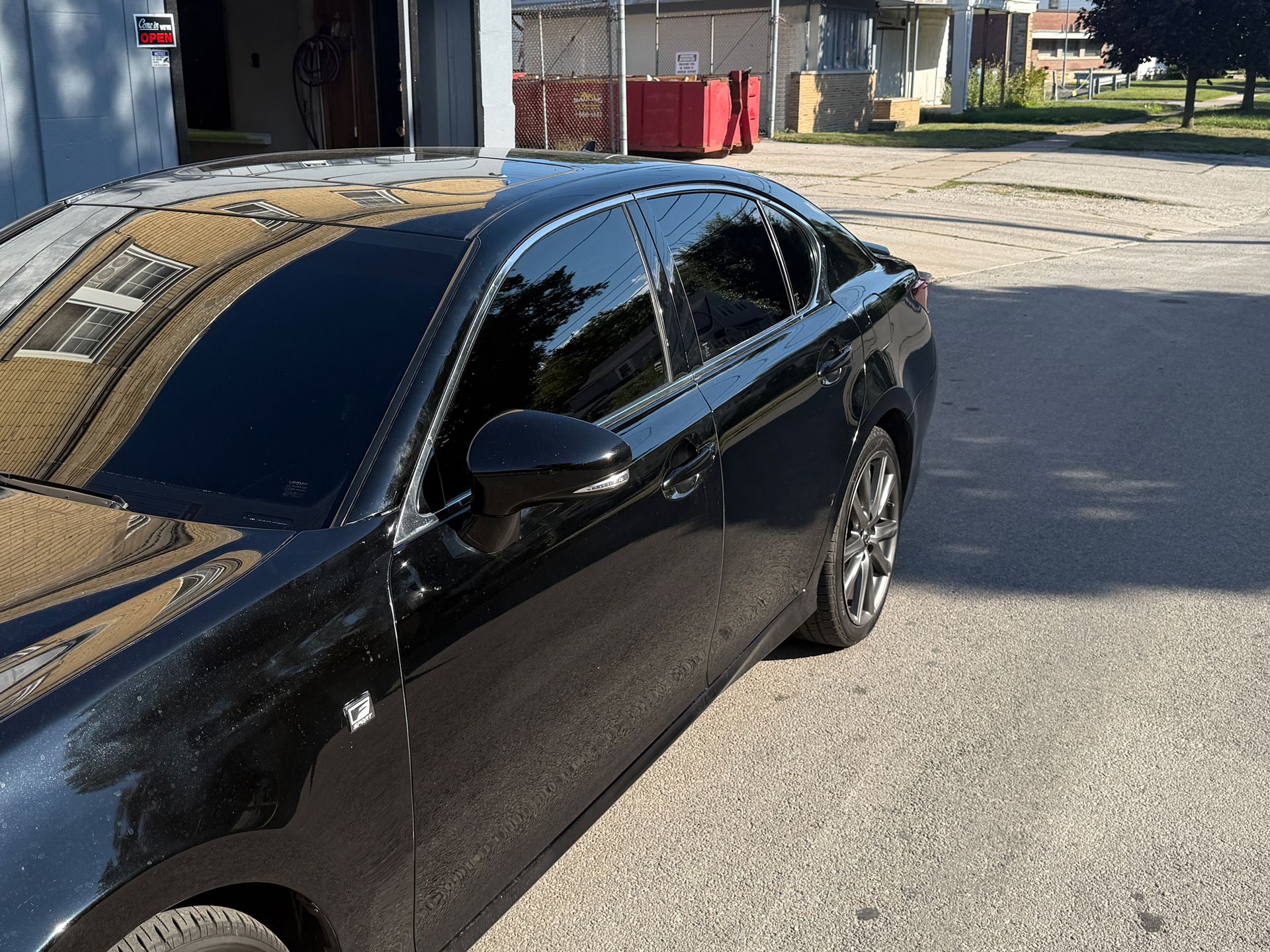 Black car with tinted windows parked on asphalt in front of a building on a sunny day.