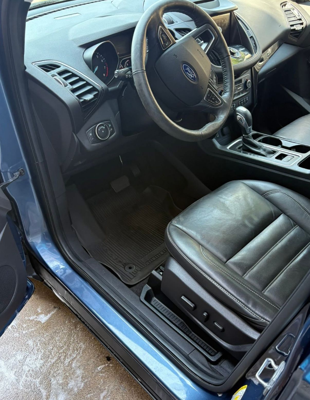 Interior view of a blue car. Black leather driver's seat, steering wheel, and dashboard.
