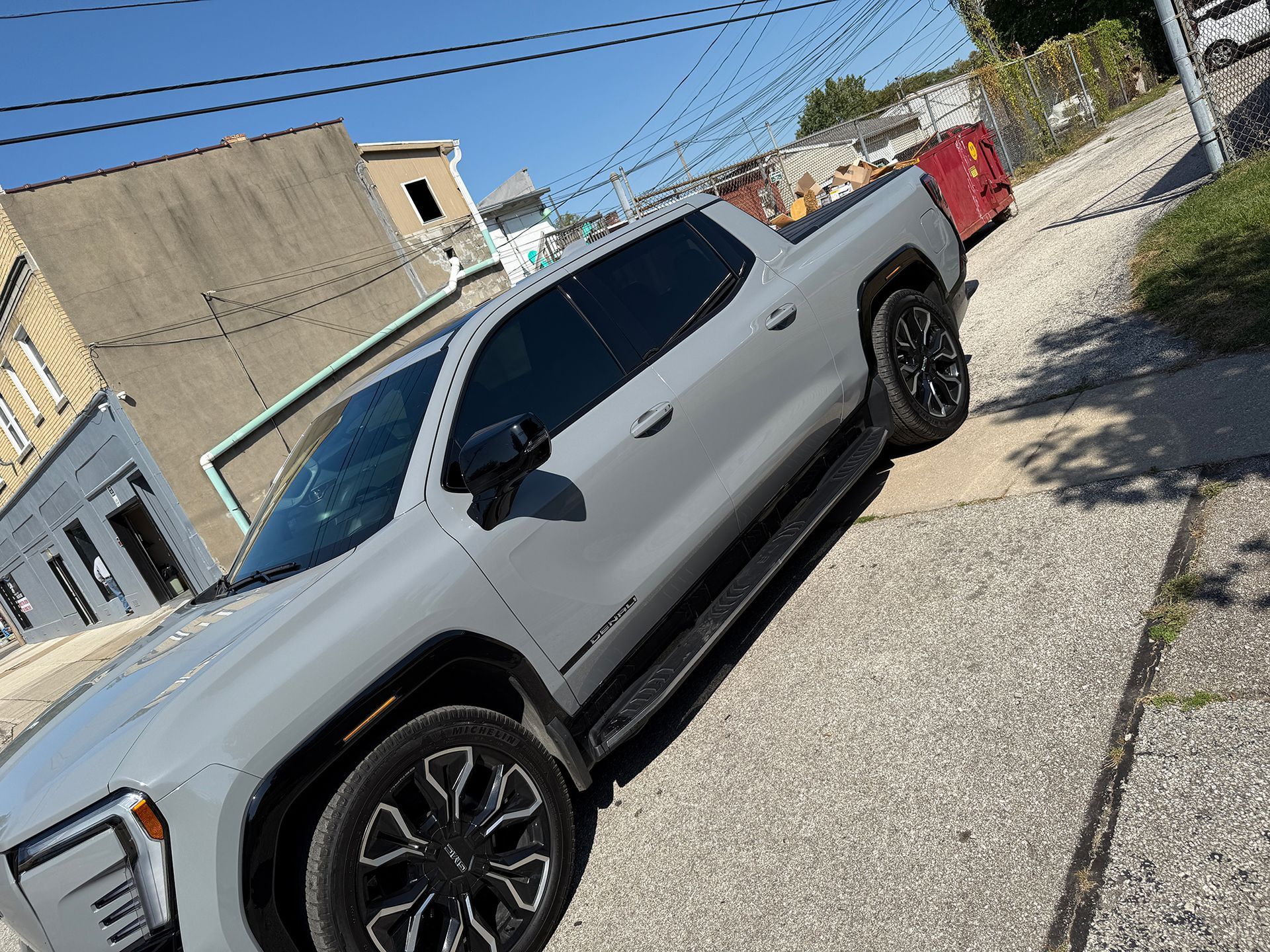 Gray pickup truck parked on a paved street next to a building on a sunny day.