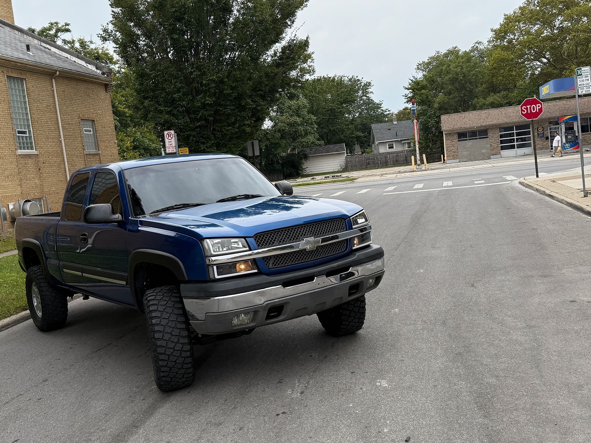 Blue pickup truck parked on a city street near a building and a stop sign.