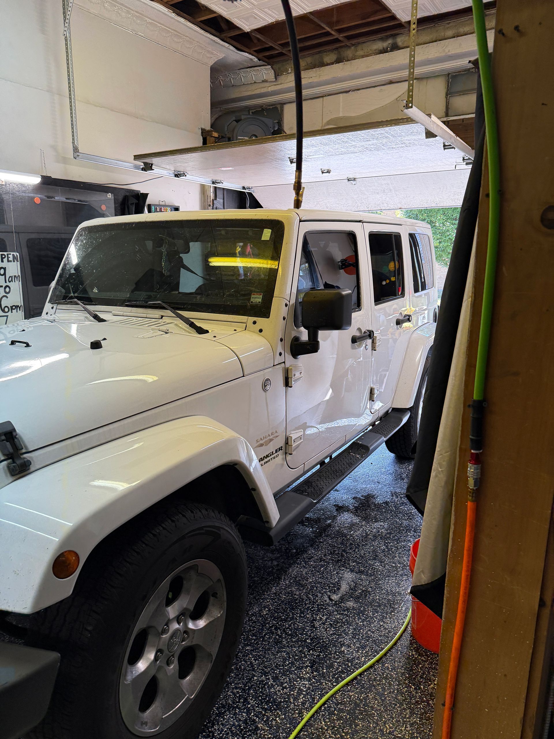 White Jeep Wrangler inside a garage with black and gray floor. Air hose and tools visible.