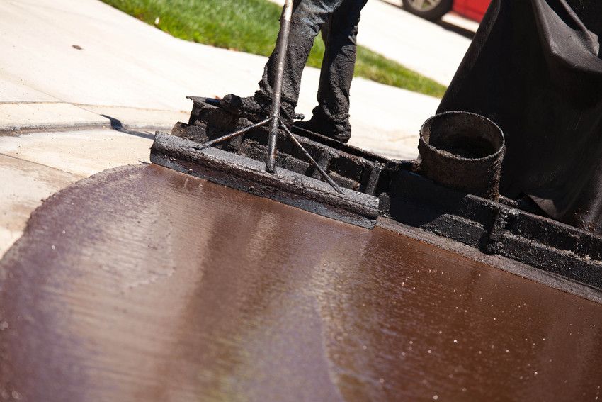 A man is spreading seal coat on a sidewalk with a broom