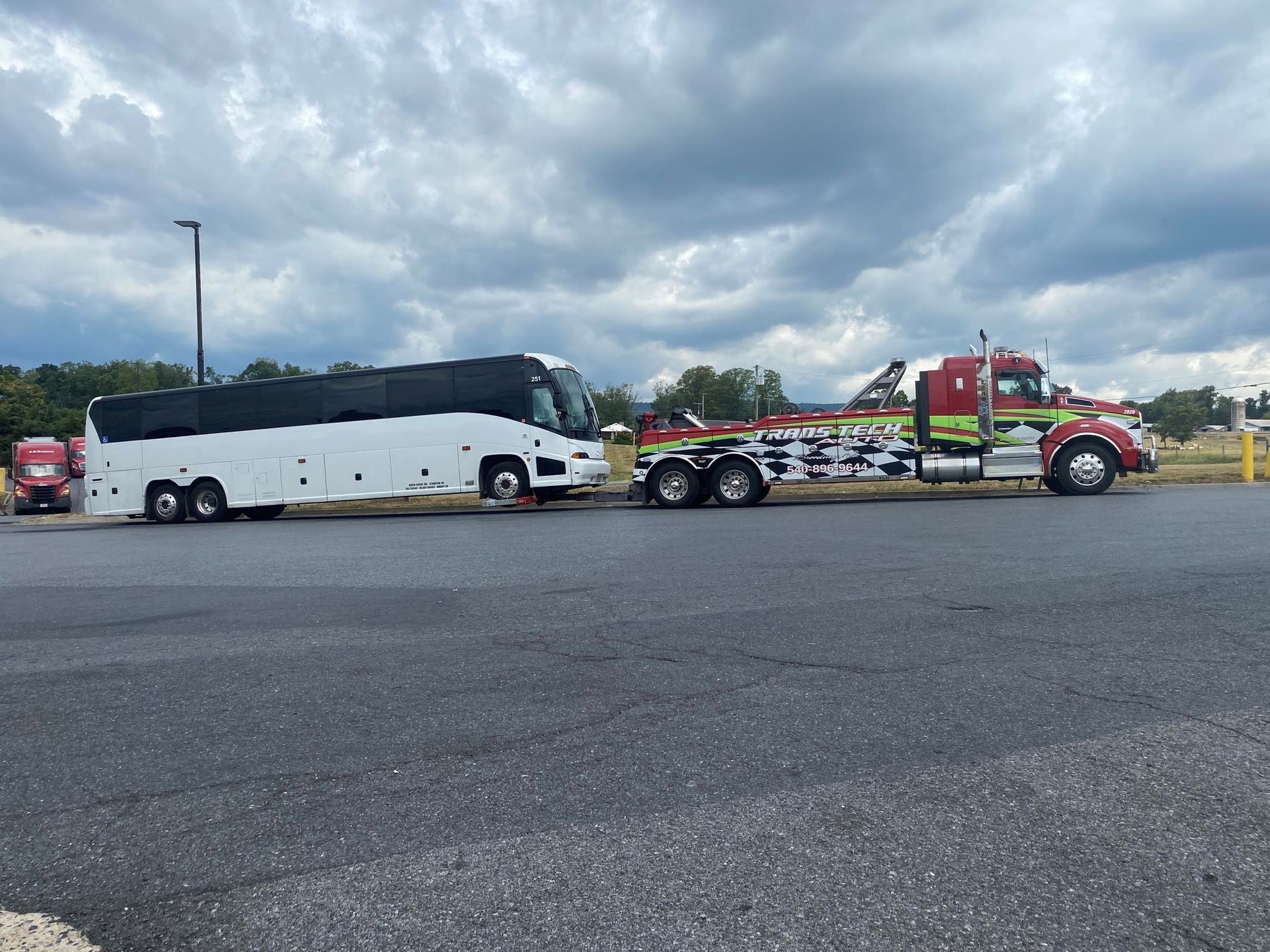 White coach bus parked beside a red tow truck in a cloudy lot