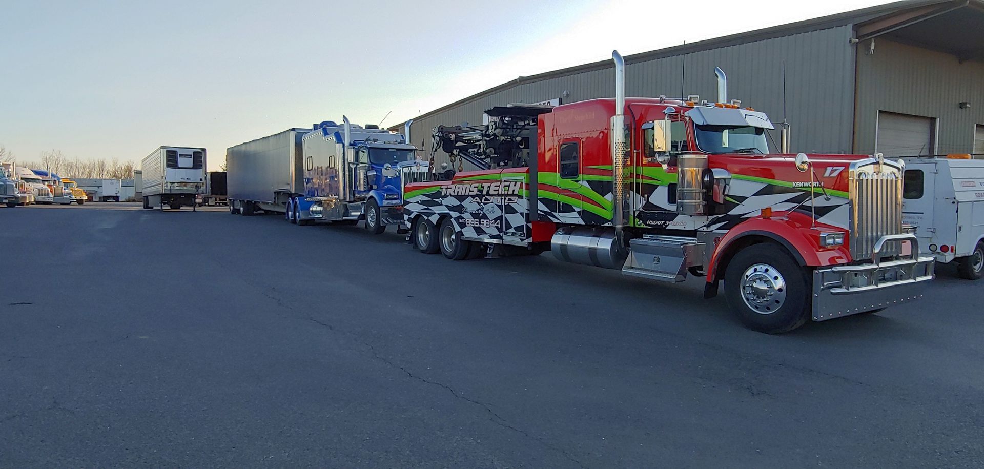 Red semi truck with trailers and equipment parked in an industrial lot at sunset