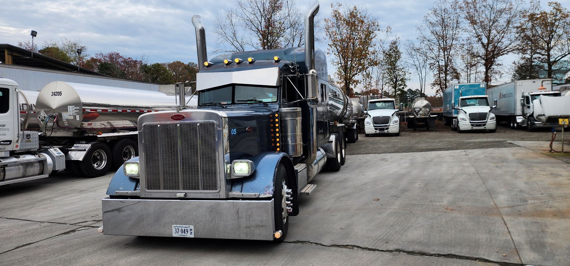 Blue semi-truck parked in a lot with several trucks in the background under a cloudy sky