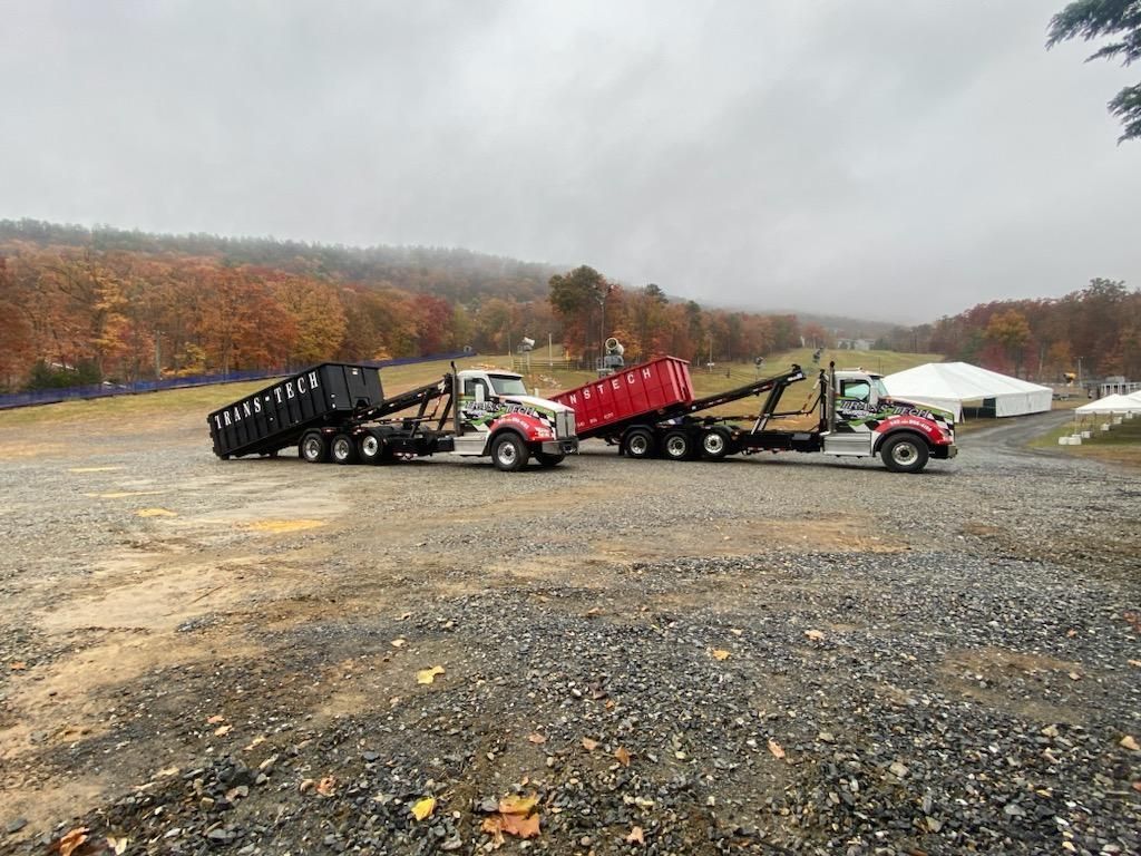 Several dump trailers lined up in a gravel lot with autumn trees and overcast sky