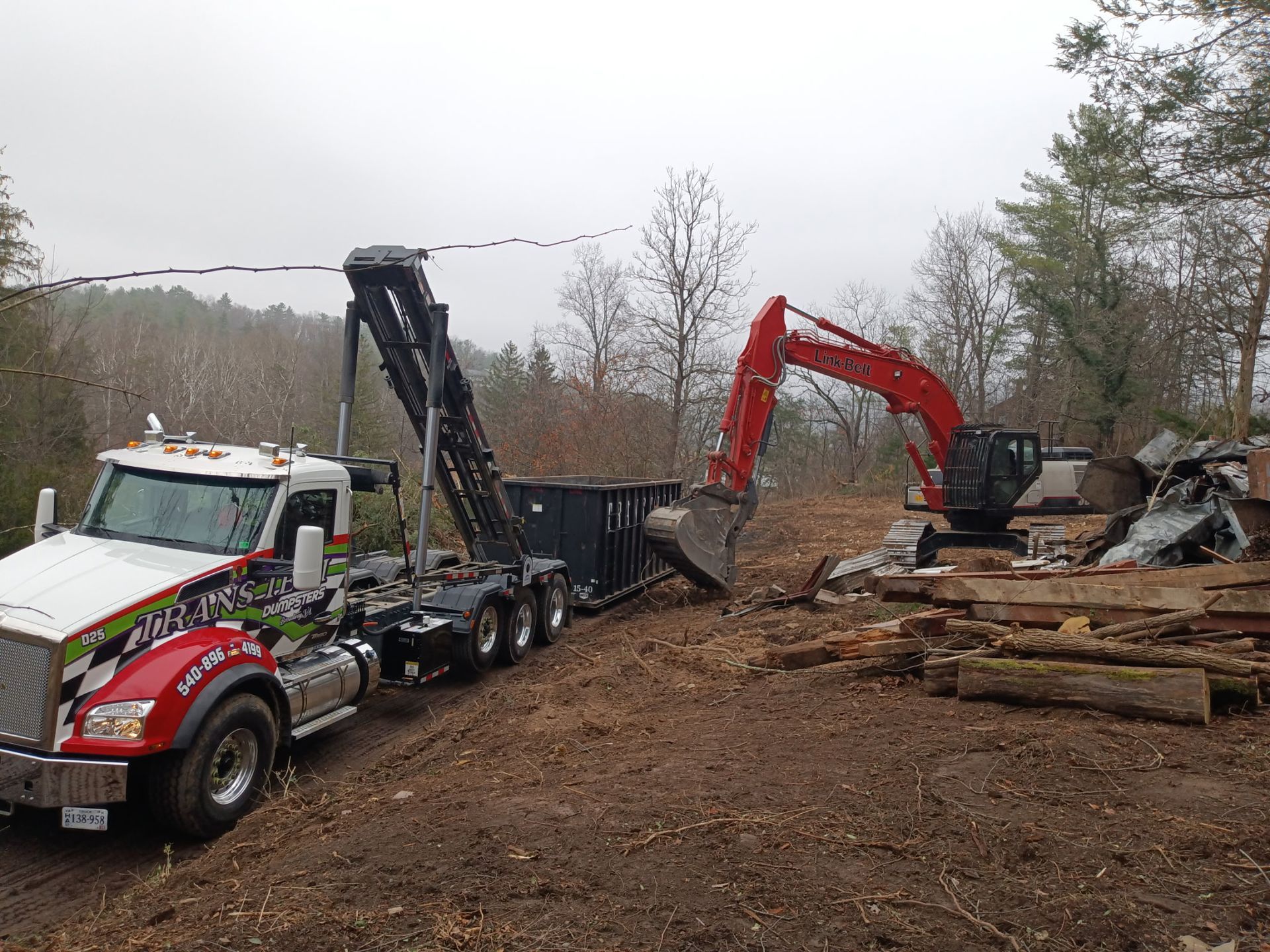 Logging trucks and excavators working in a muddy clearing with cut logs piled nearby.