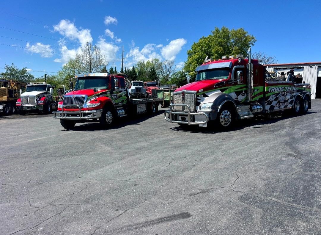 Red tow trucks and service vehicles parked on a gravel lot under a blue sky with clouds