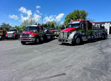 Red tow trucks and service vehicles parked on a gravel lot under a blue sky with clouds