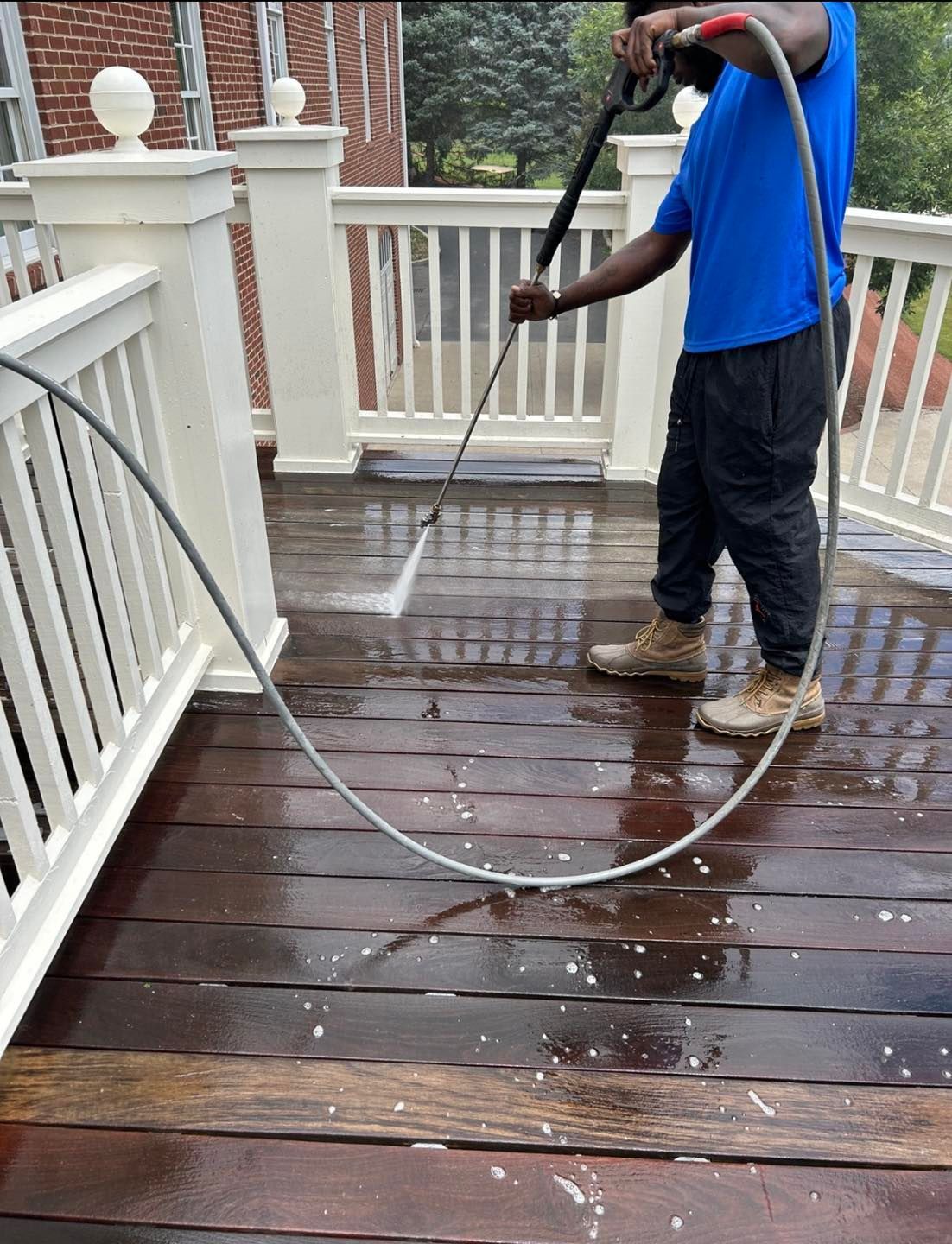 A man is cleaning a wooden deck with a high pressure washer.