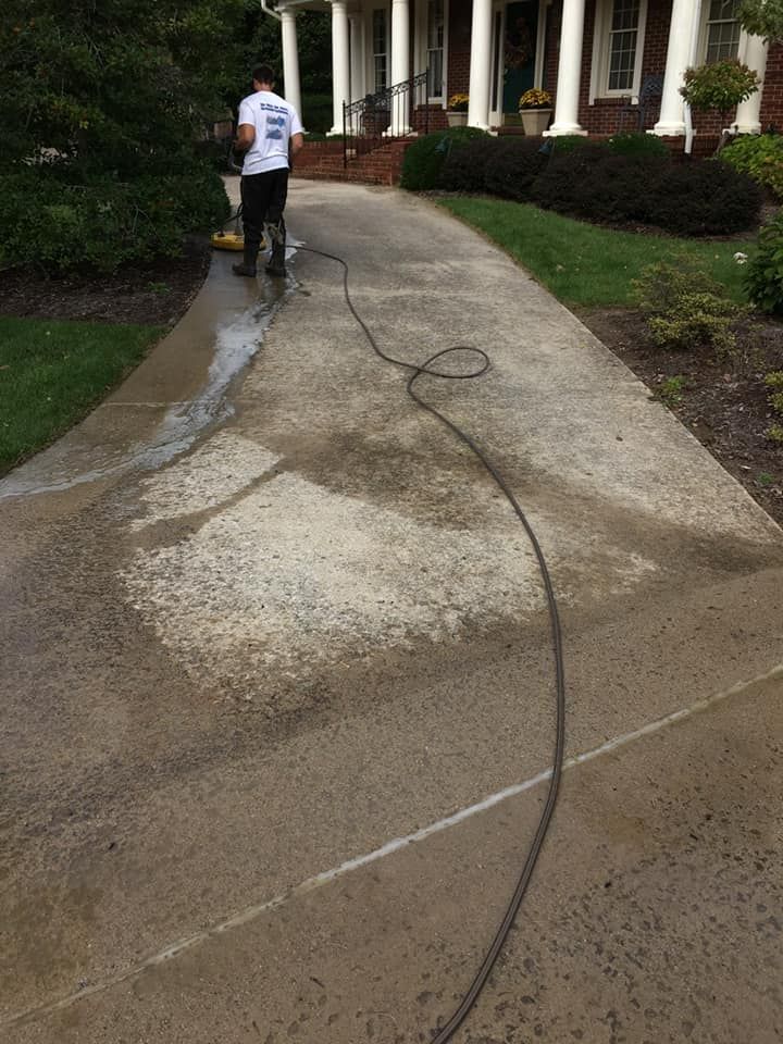 A man is using a pressure washer to clean a driveway in front of a house.