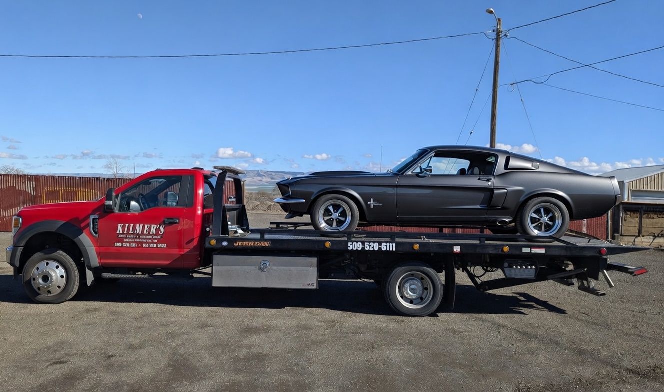 Red tow truck with a gray classic muscle car on its flatbed
