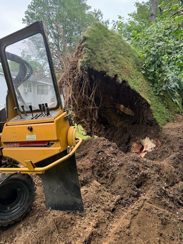 A yellow tractor is cutting a tree stump in the dirt.