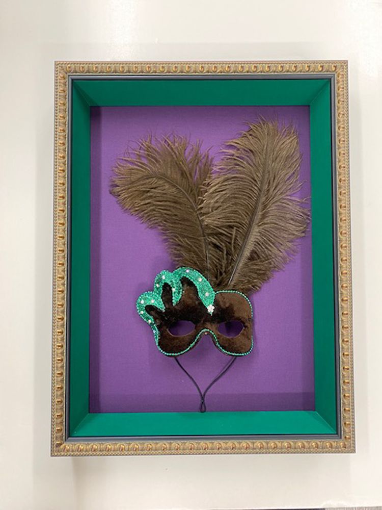 A framed picture of a mask with feathers on it.