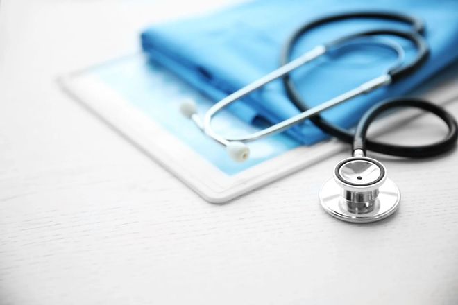 Stethoscope on blue scrubs and a tablet, on a white surface.