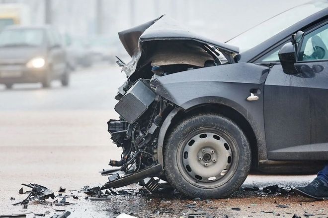Black car heavily damaged after a collision on a city street.