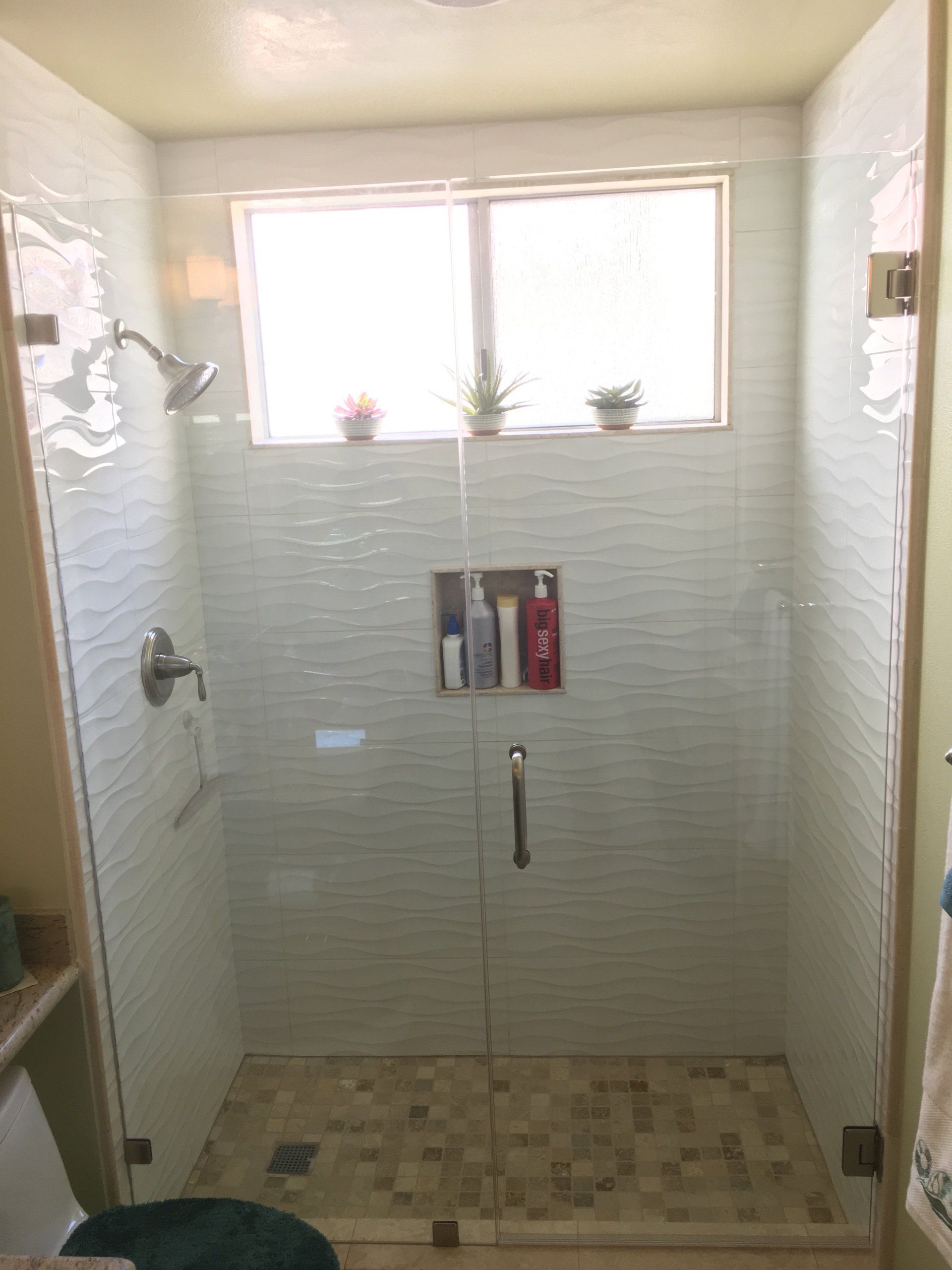A bathroom with a walk in shower with a glass door and a window.