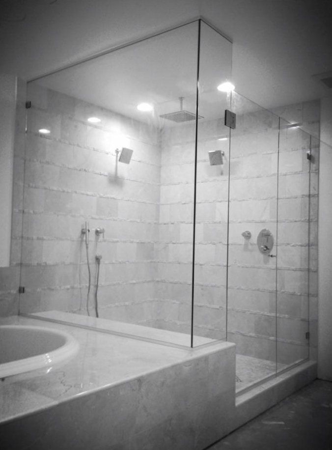 A black and white photo of a bathroom with a walk in shower and a bathtub.
