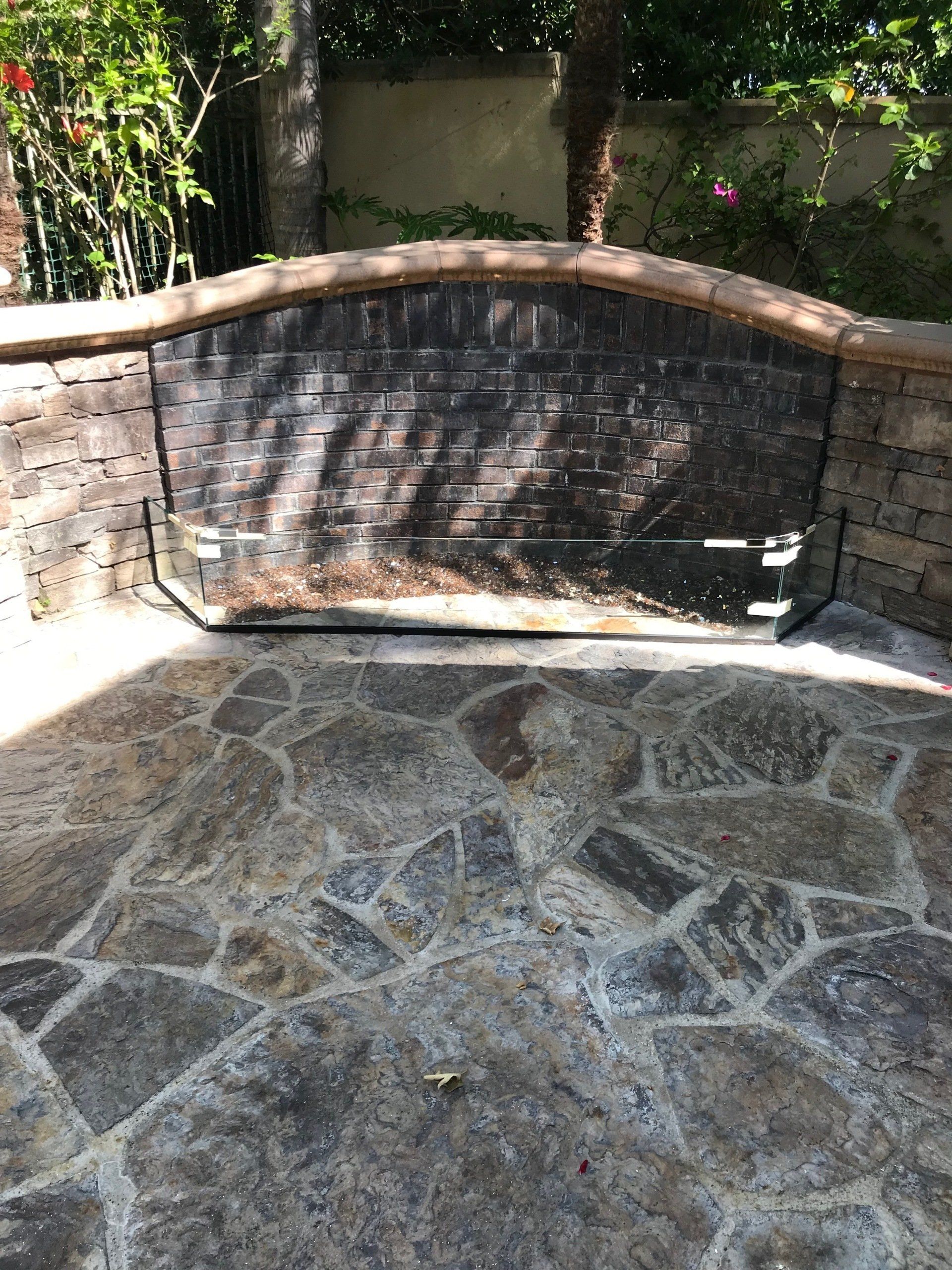 A stone patio with a brick wall and a bench.