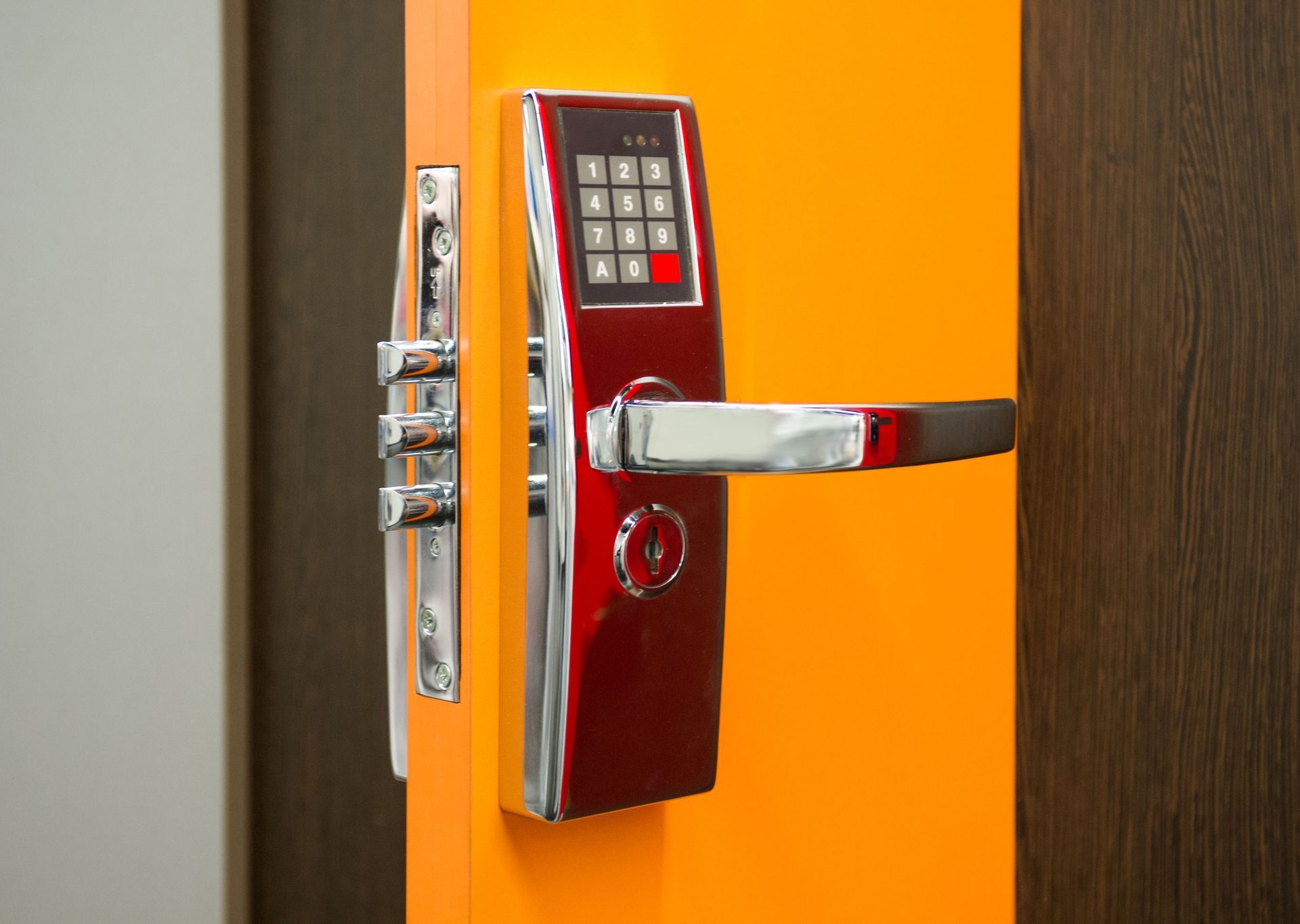 Red and silver smart door lock with keypad and handle on an orange door.