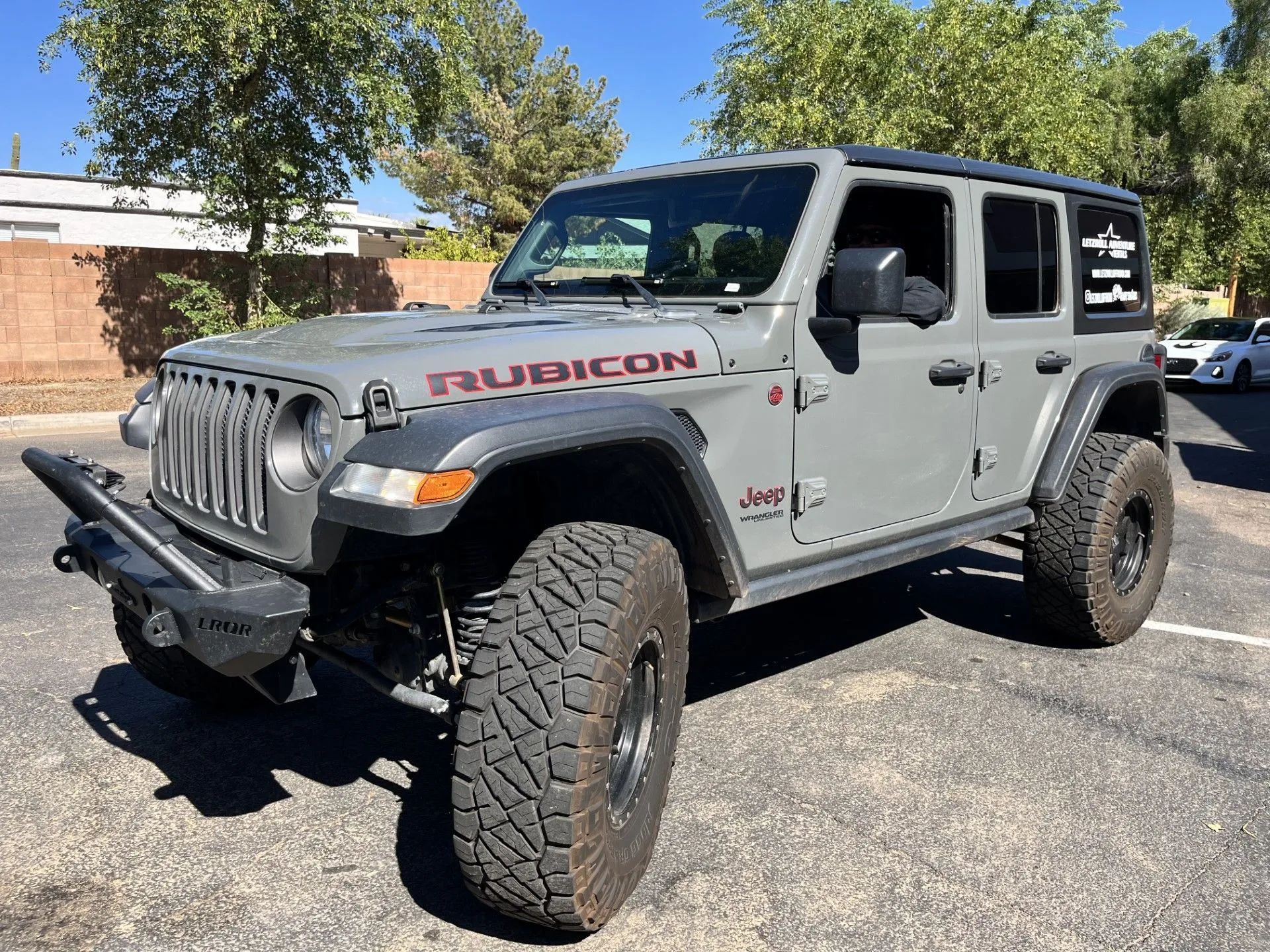Gray Jeep Wrangler Rubicon parked on asphalt, with large tires and a custom front bumper.