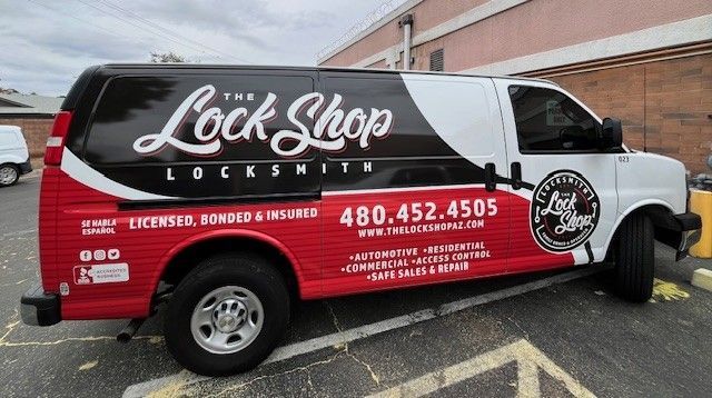 A red, black, and white van with "The Lock Shop Locksmith" logo and contact info on the side.