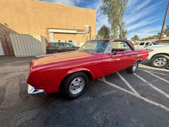 Red classic car parked in front of a building; daytime.