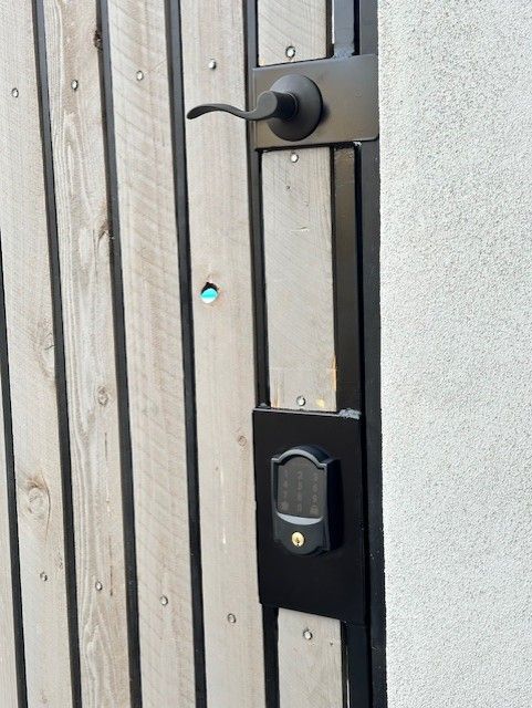 Wooden gate with black metal frame, door handle, and keypad lock.