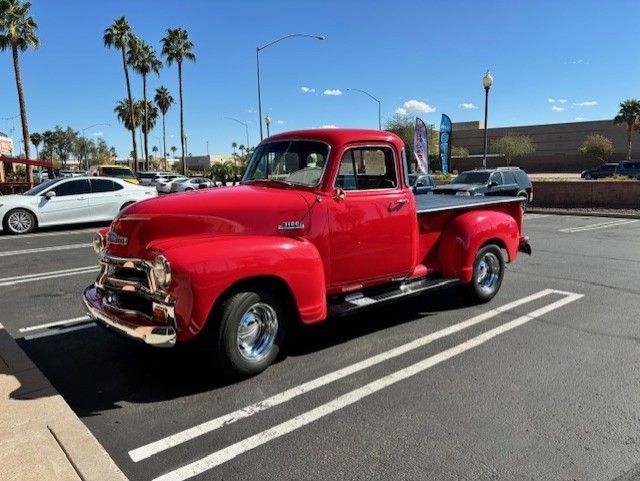 Red vintage Chevrolet pickup truck parked in a lot under a blue sky.
