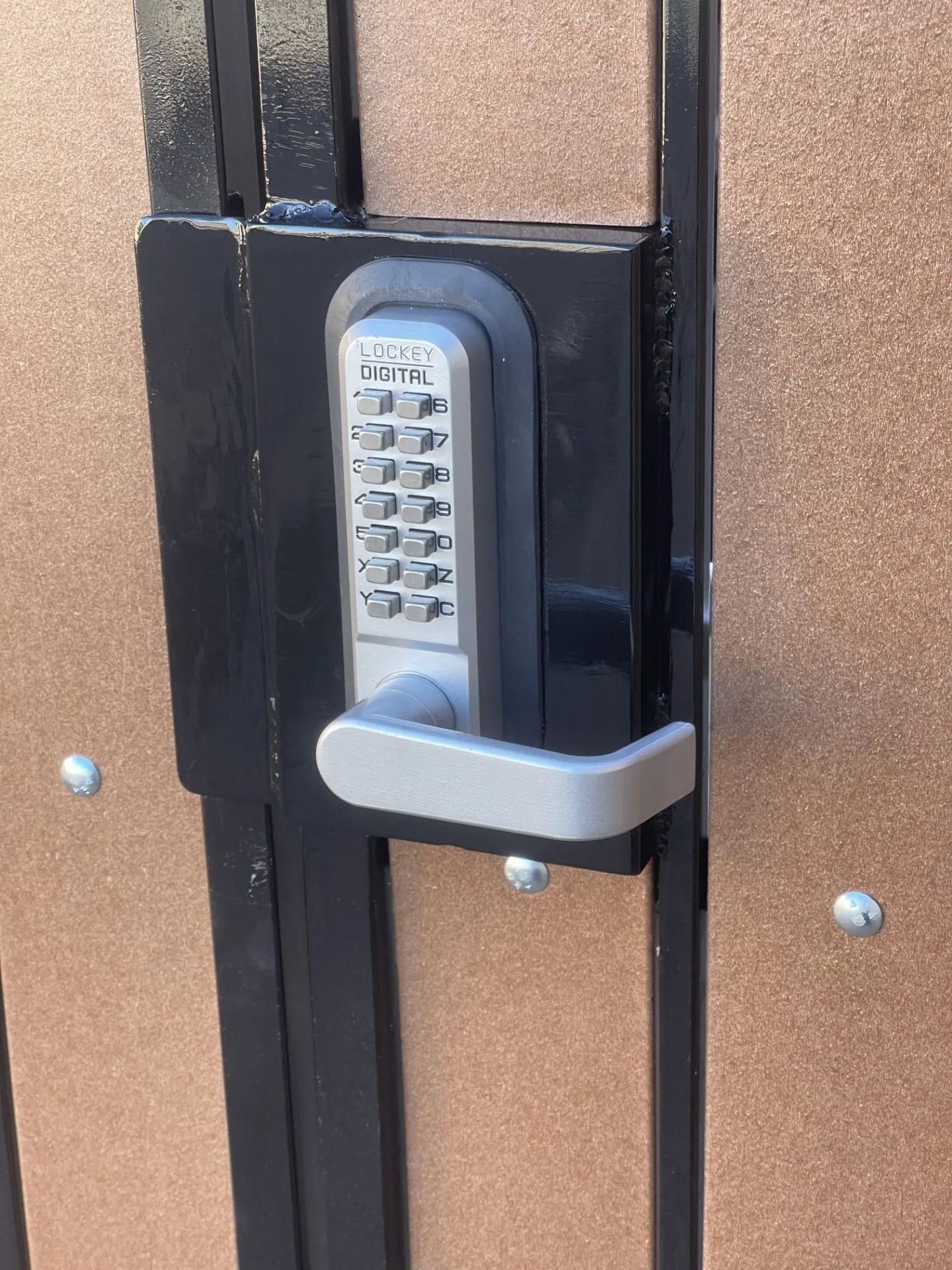 A keypad lock with a handle on a brown gate.