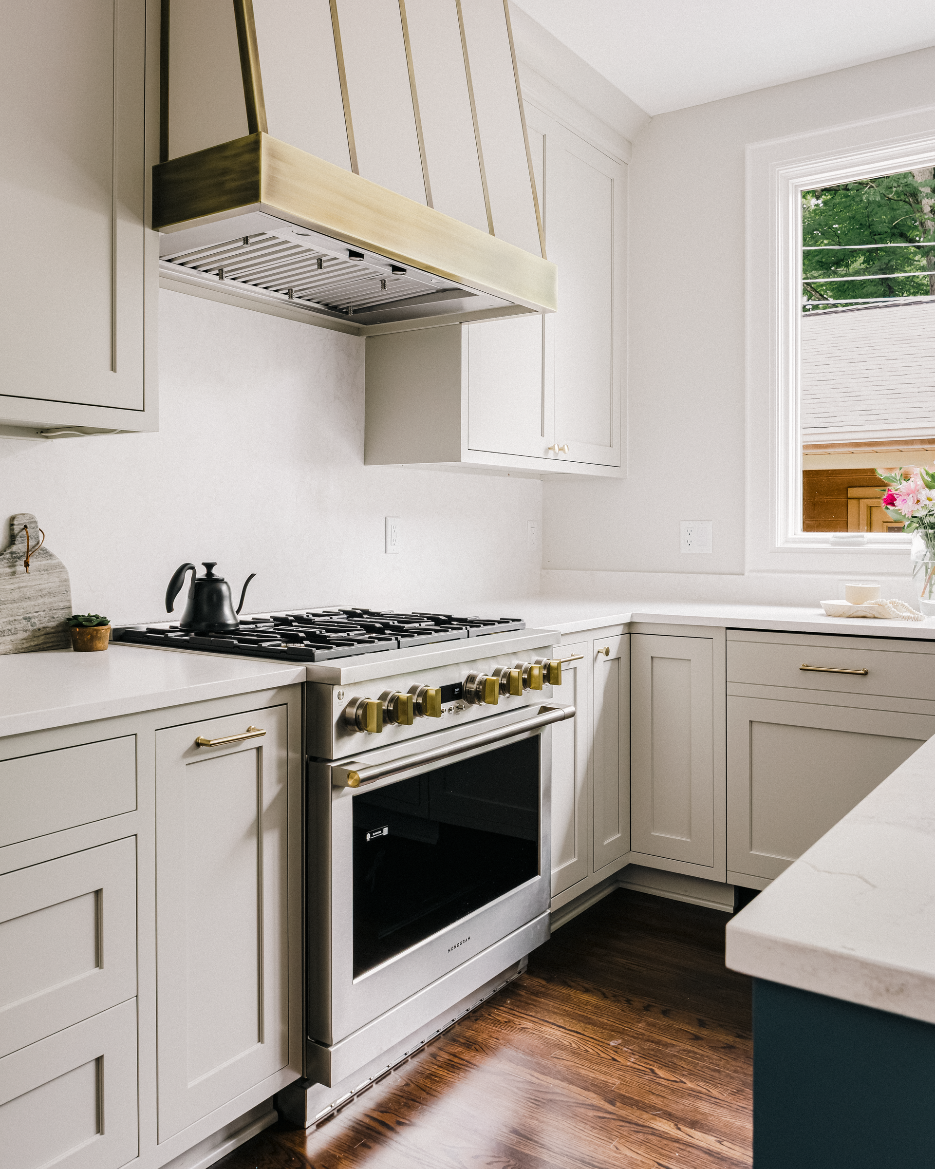 White kitchen with gold accents, stovetop, hanging range hood, and window.